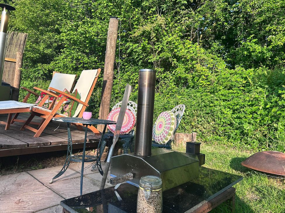 A garden with an outdoor stove and wooden chairs at Cozy Cabin Retreat near Chepstow