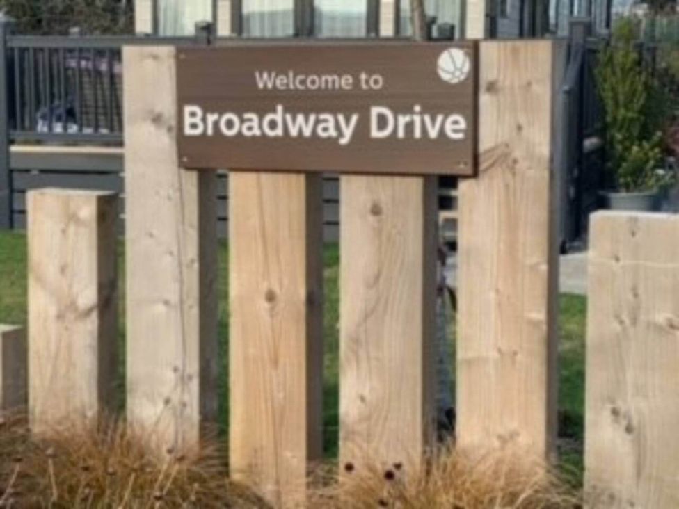 A welcome sign for Broadway Drive with a wooden fence in an outdoor area