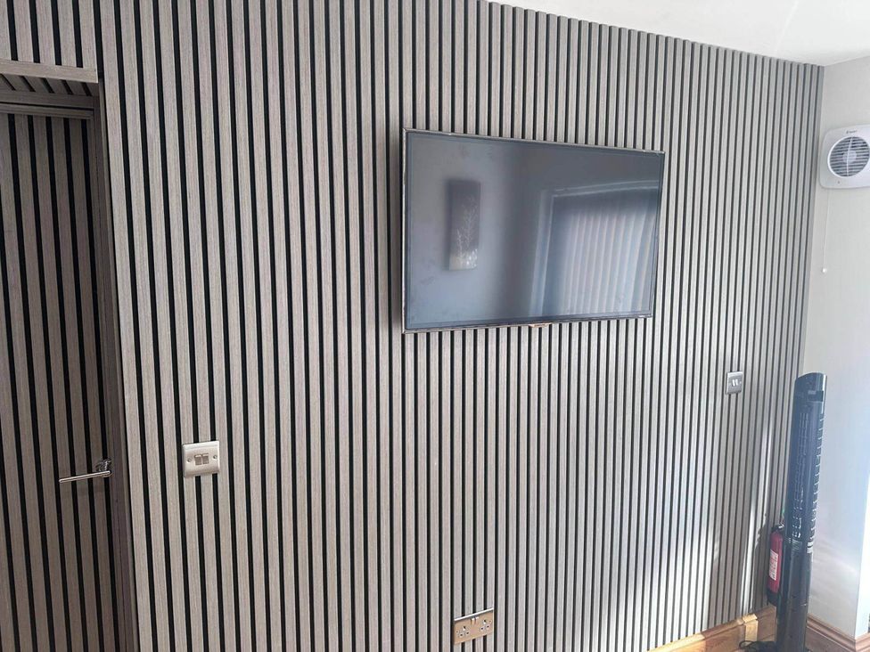 A living room with a television mounted on a striped wall at Beautiful 1-Bed studio in Penrith