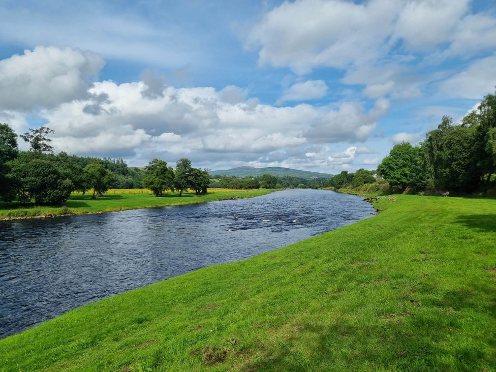 A river flowing alongside green grass and trees at The Coal Office, Aberlour
