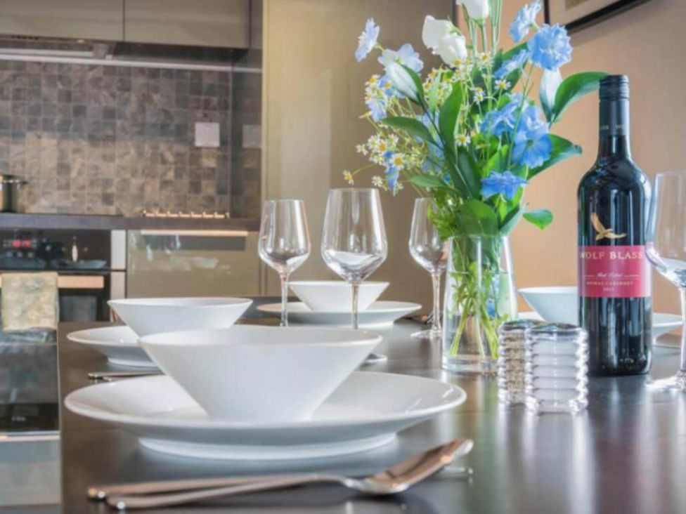 A dining room table set with plates, glasses, and a wine bottle at Sedbergh Penthouse - KingBed - Tv - Wifi Sedbergh