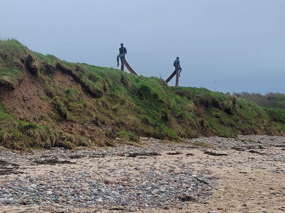 Two statues on a grassy hill at the beach
