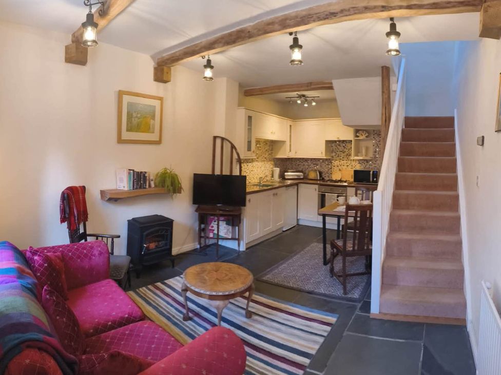 A living room with a sofa, coffee table, and kitchen area at Cosy Cottage for two in the centre of Sedbergh
