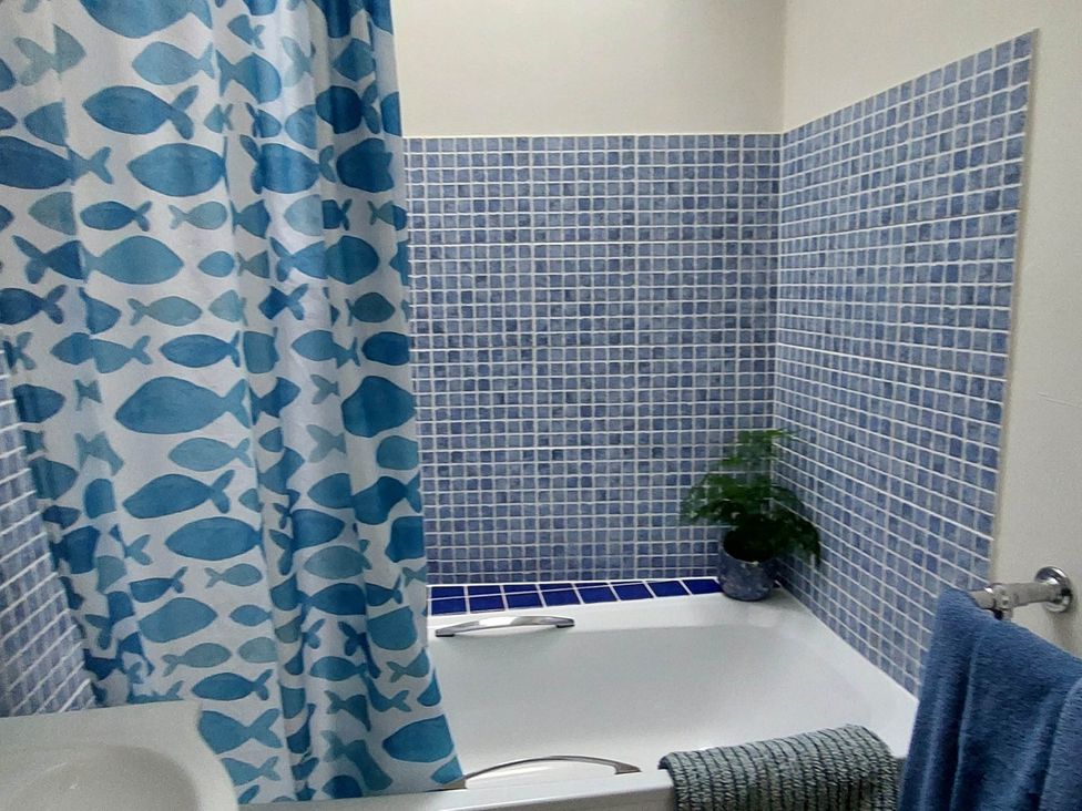A bathroom with a bathtub, fish patterned shower curtain, and tiled wall at Cosy Cottage for two in the centre of Sedbergh