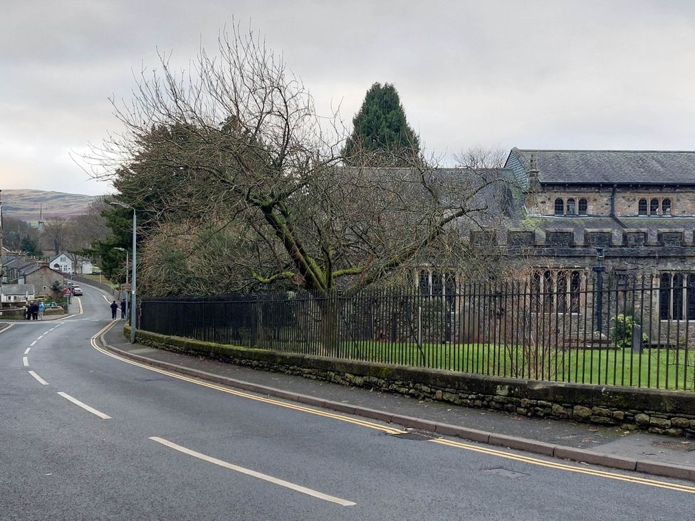 A view of a road with a fence and buildings at Cosy Cottage for two in the centre of Sedbergh