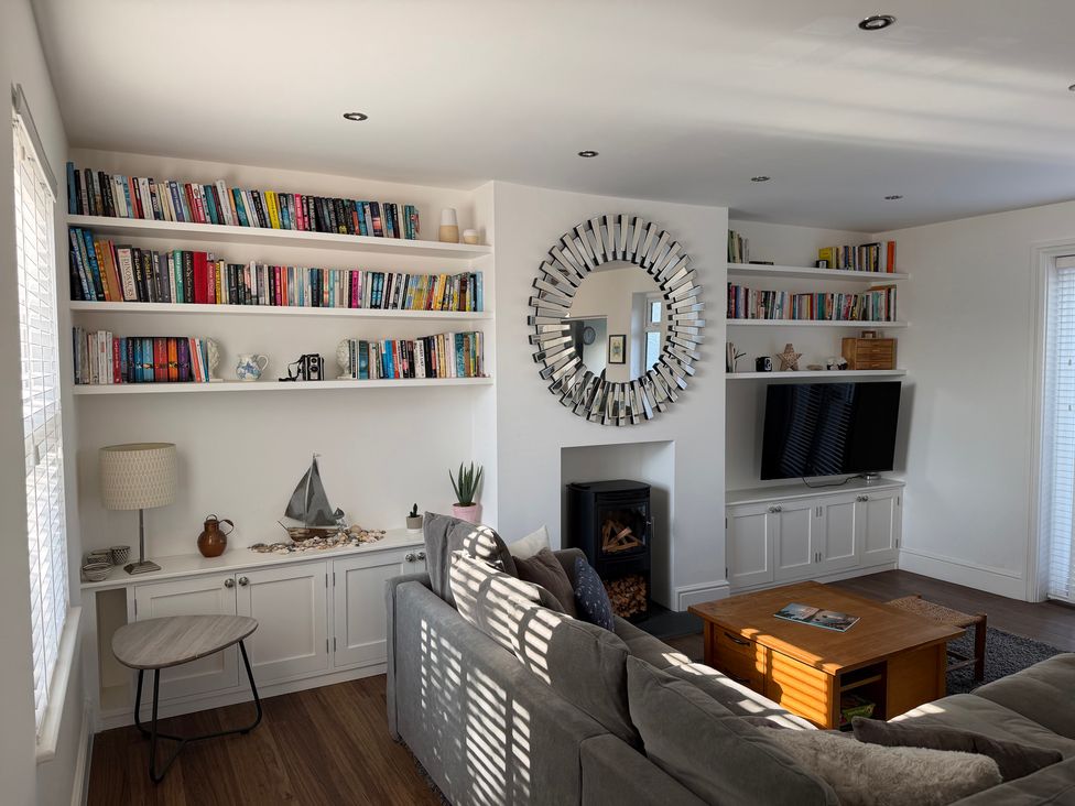 A living room with a bookshelf, tv, and fireplace at Lorrell in Salcombe