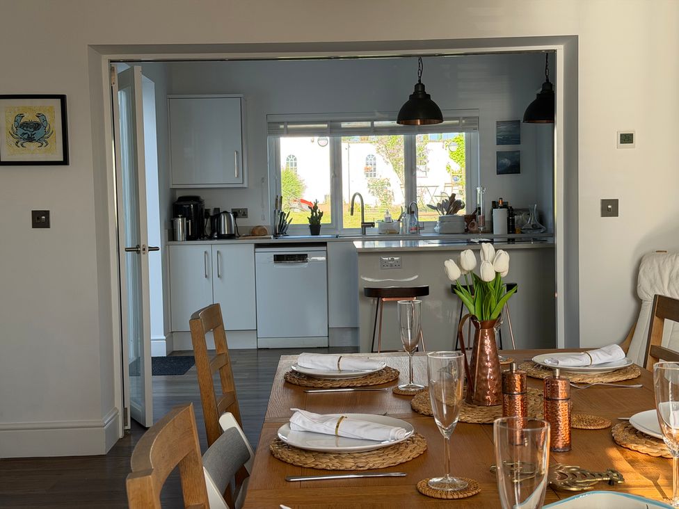 A dining room with a table set for dinner and a view of the kitchen at Lorrell in Salcombe