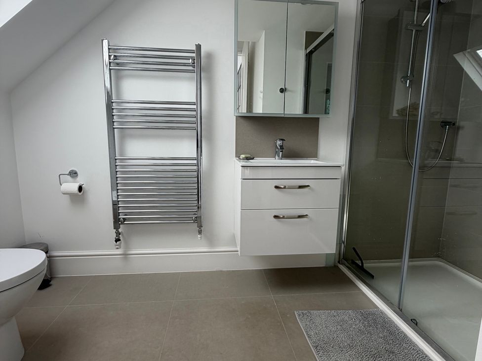 A bathroom with a sink, mirror, shower and towel radiator at Lorrell in Salcombe
