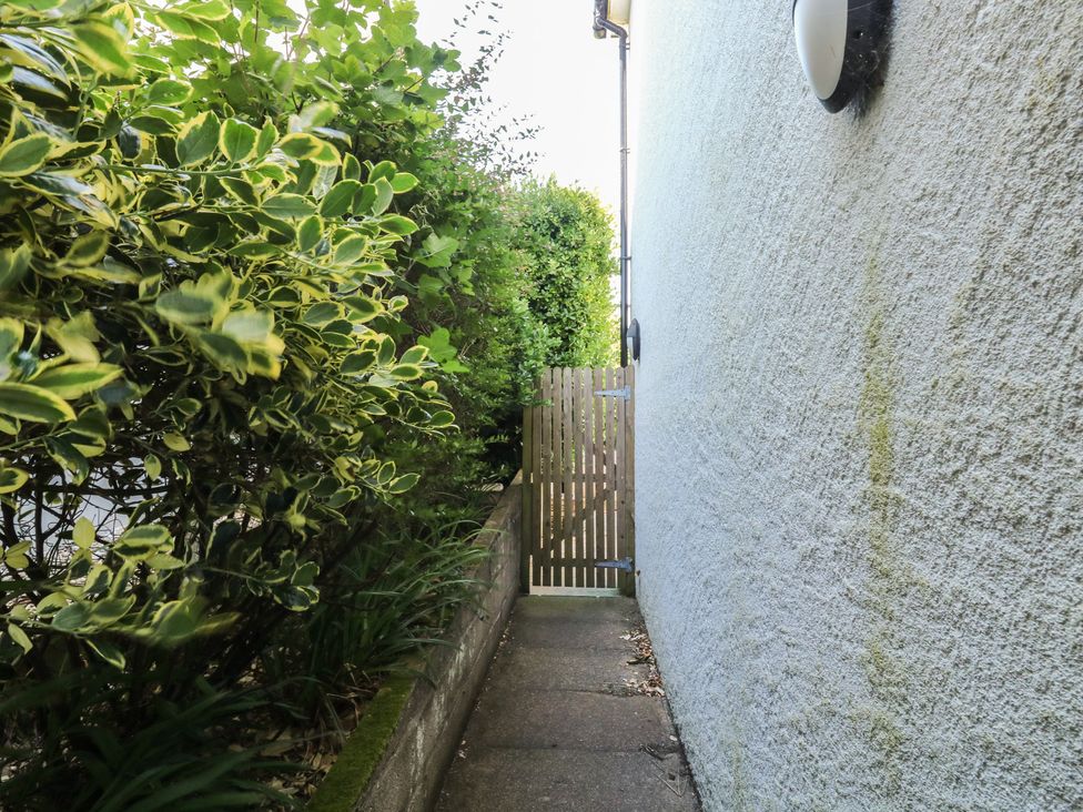 A pathway next to a wall with bushes and a gate at Lorrell in Salcombe