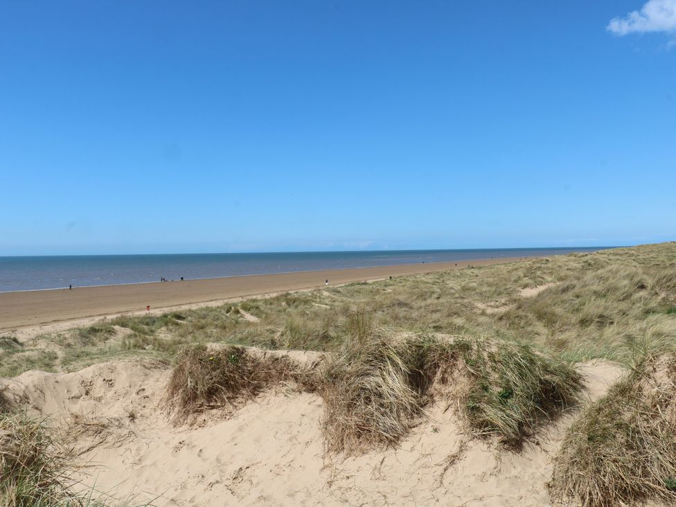 A beach with sand and grass under a blue sky at Apartment 2 in Lytham St. Annes