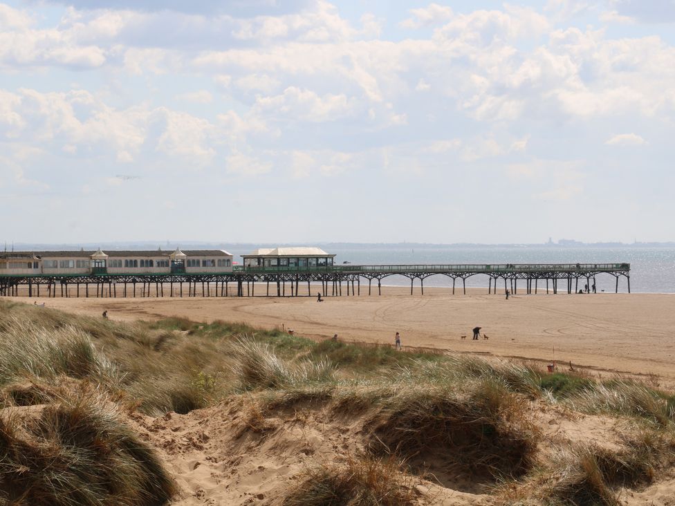 A beach with a pier and people walking at Apartment 2 in Lytham St. Annes