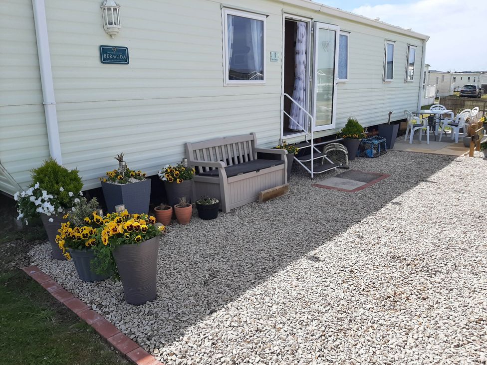 An outdoor area with a caravan, bench, and flower planters at Taid's Retreat Silversands Cove beach lossiemouth