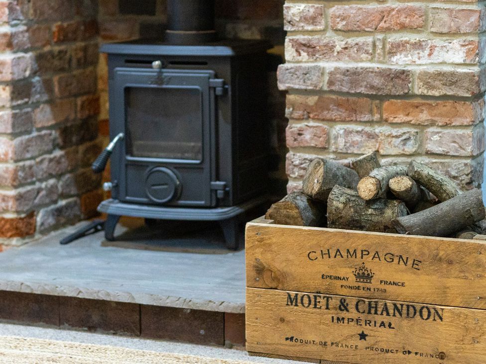 A living room with a wood stove and logs in a wooden crate at The Groom's Cottage, at Ivy House near Louth