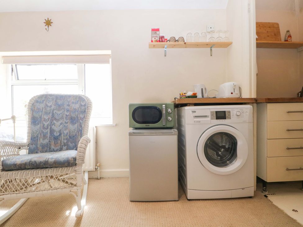 A utility room with a rocking chair, washing machine, fridge, and microwave at Daisy Cottage 22 Chalkpit Terrace in Dorking