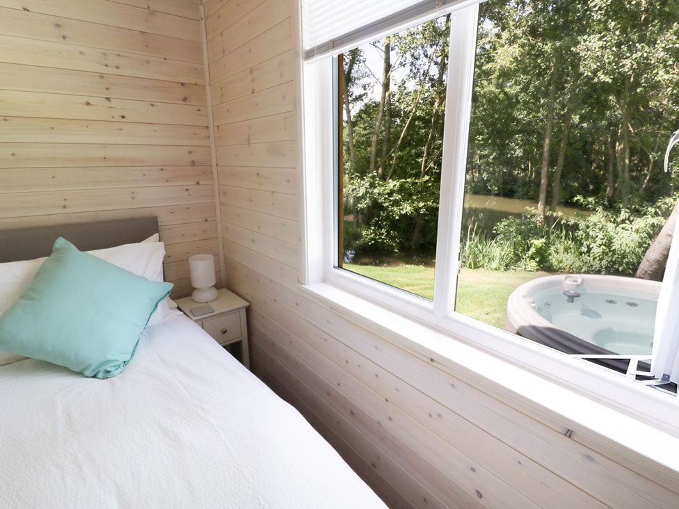 A bedroom with a bed and a window showing a hot tub and trees at Skylark in Ross-on-Wye