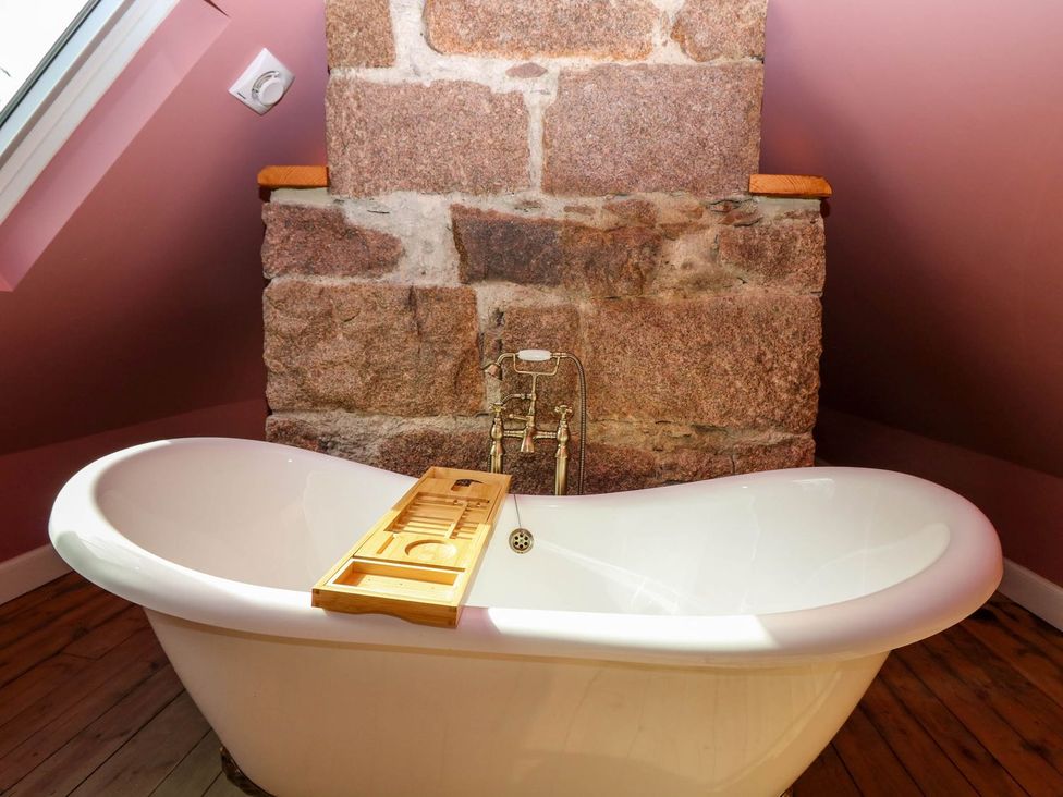 A bathroom with a bathtub against a stone wall at Evansford in Ballater