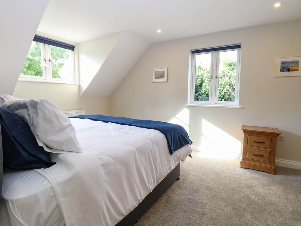 A bedroom with a bed, nightstand, and windows at Bramley Cottage in Worlingham