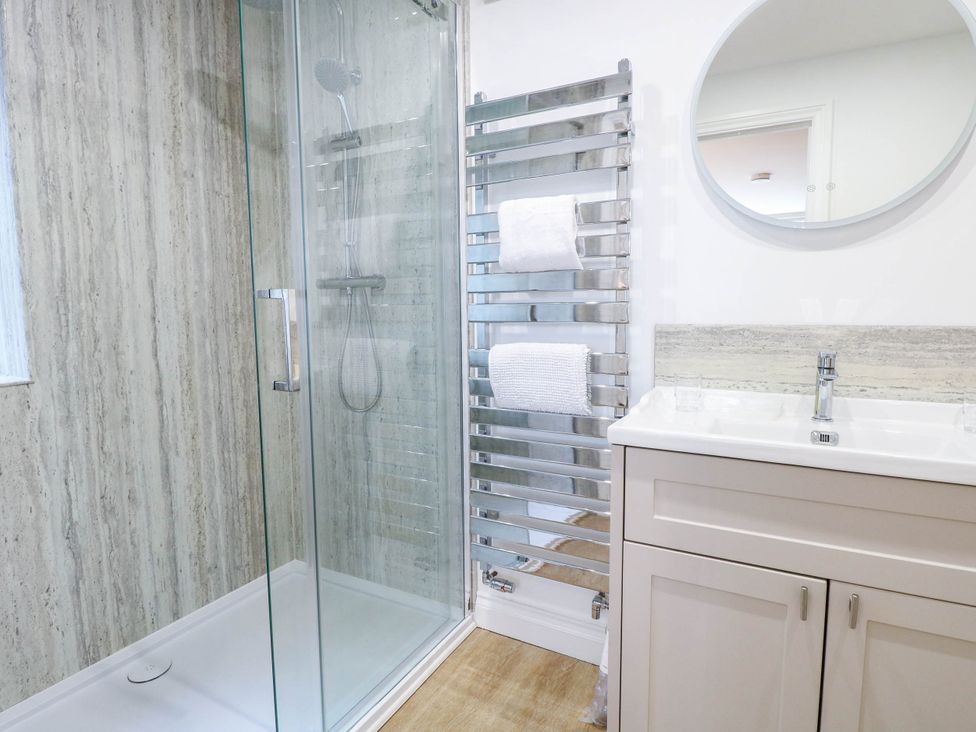 A bathroom with a shower, towel rail, sink and mirror at Bramley Cottage in Worlingham