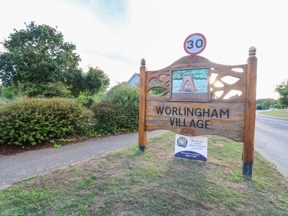 A village sign for Worlingham Village with surrounding greenery and road