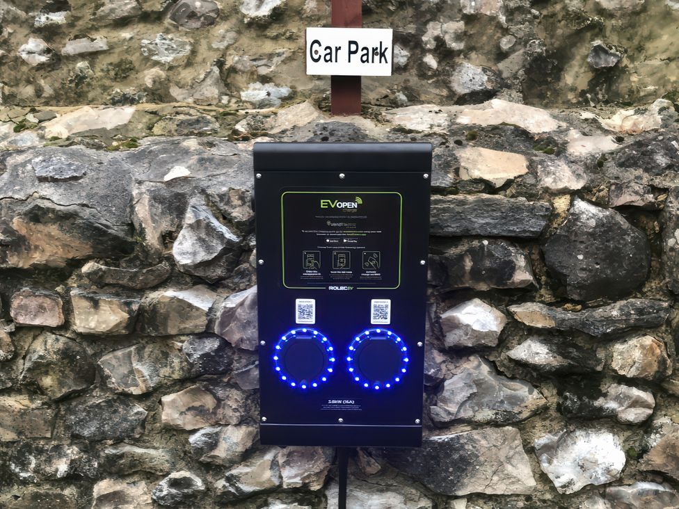 An electric vehicle charger mounted on a stone wall at Cider House in Hawkchurch