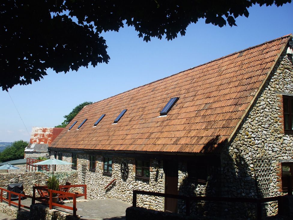 An outdoor view of a stone house with a tiled roof and windows at Cider House in Hawkchurch