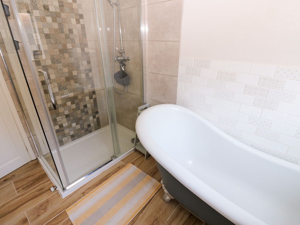 A bathroom with a bathtub and a shower in a tiled space at 14 The Porch Barton