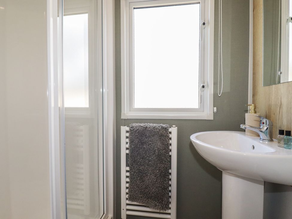 A bathroom with a shower, sink, and window at Shamrocks Cove Caravan