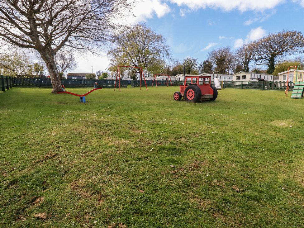 An outdoor play area with a swing set and a toy tractor at Shamrocks Cove Caravan