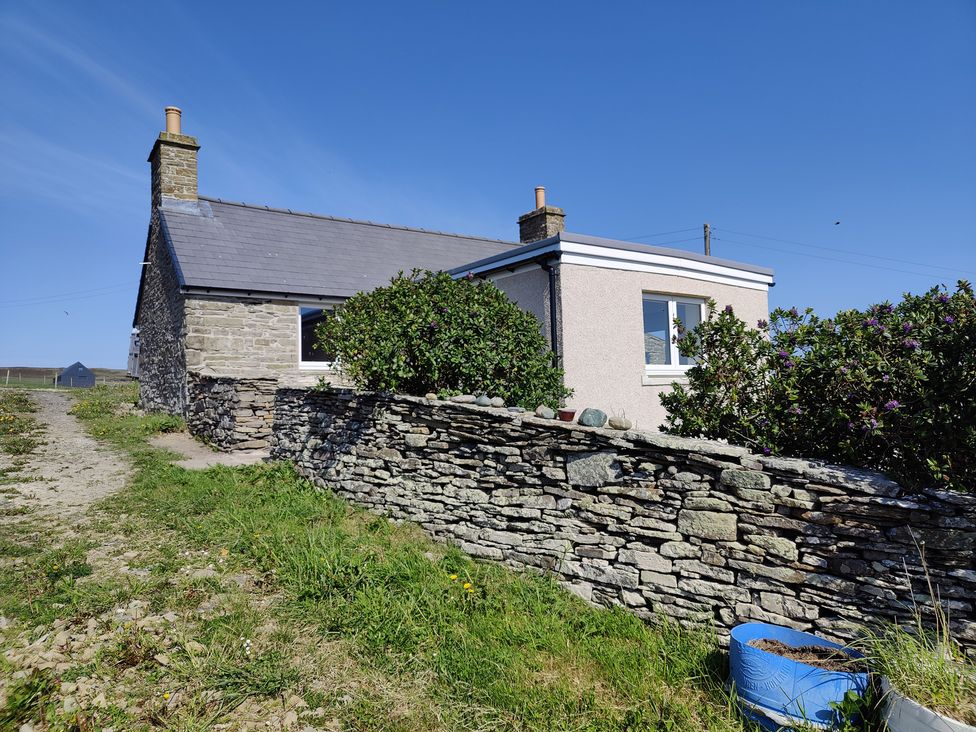 A cottage with a stone wall and grass outdoor area at Rousay Cottage in Rousay, Orkney Islands