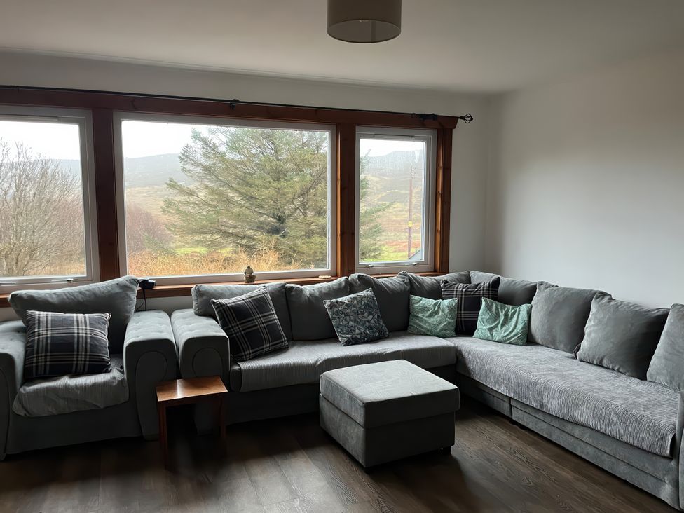 A living room with a large sofa and windows at Woodview in Isle of Barra
