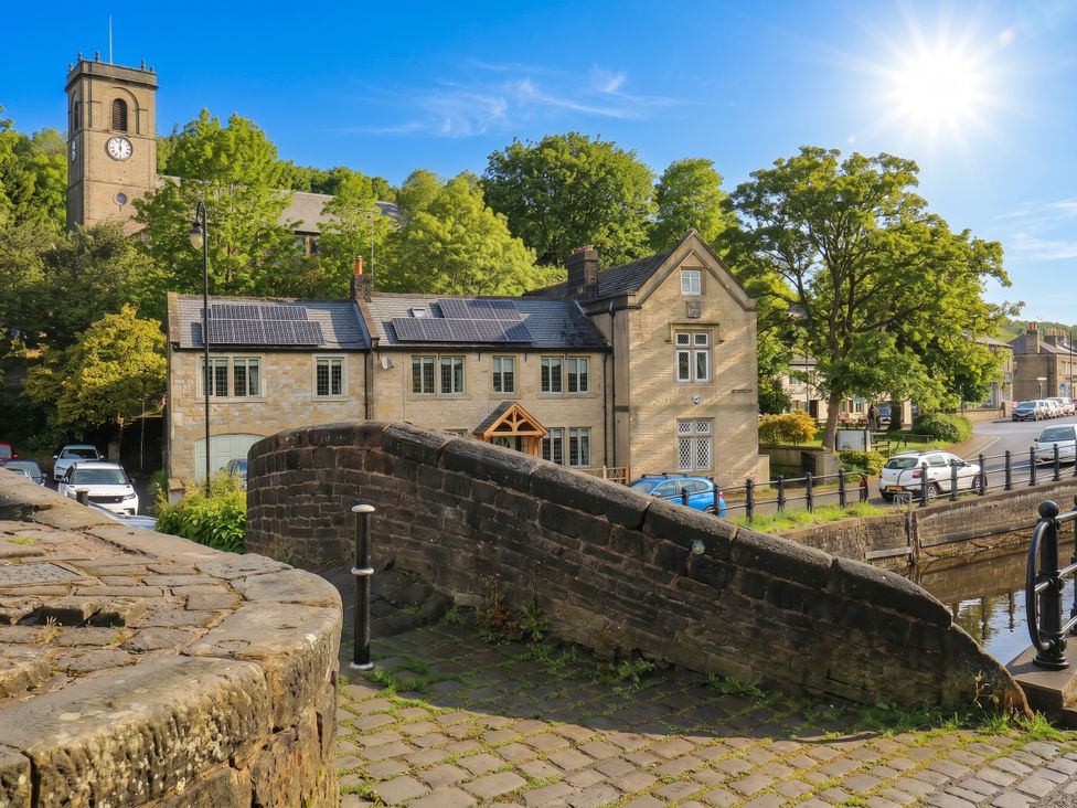 A building with a clock tower and trees at No.1 Spa Mill Lodge in Slaithwaite