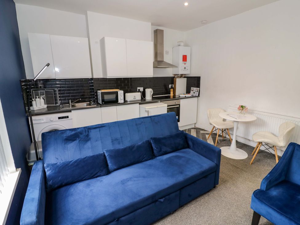 A living room with a blue sofa and kitchen area at 1C Highfield Road - 2 bed Rowley Regis