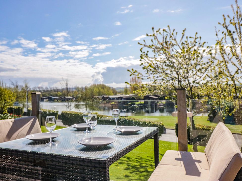 An outdoor dining setup with table and chairs overlooking a lake at Borwick Heights 17 Carnforth