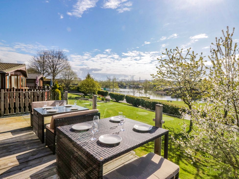 An outdoor dining area with a table and chairs overlooking a lake at Borwick Heights 17, Carnforth
