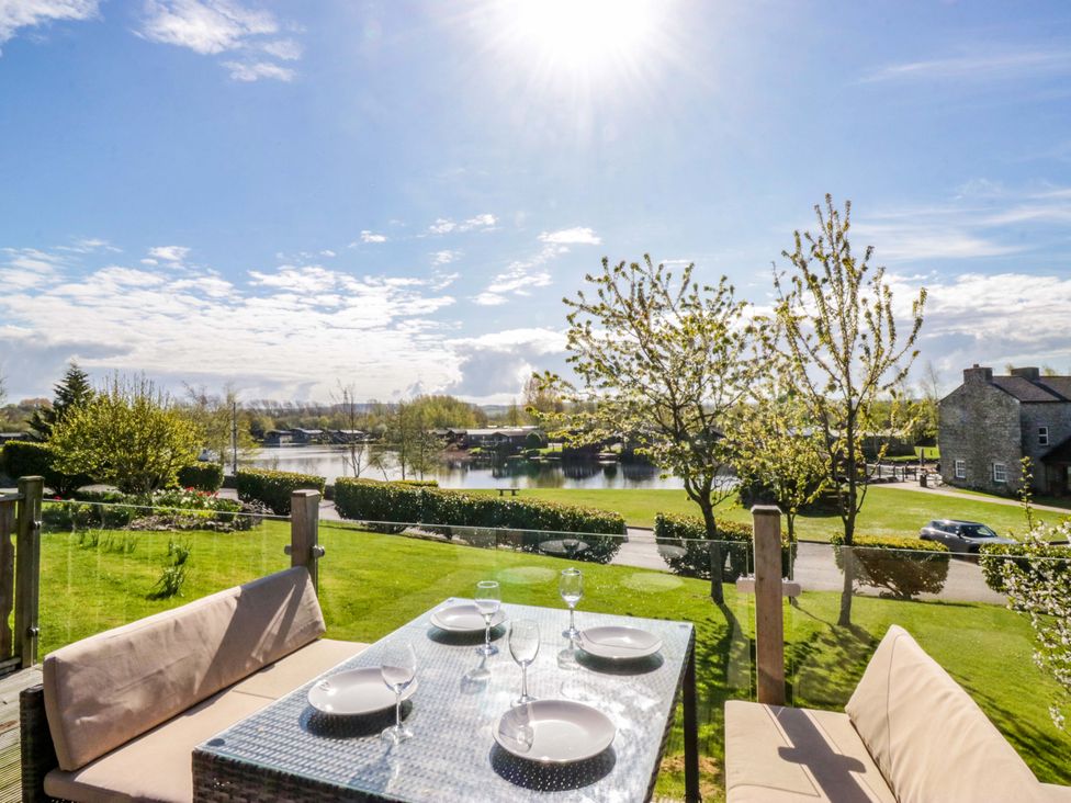 A garden with a dining table and chairs overlooking a lake at Borwick Heights 17 in Carnforth