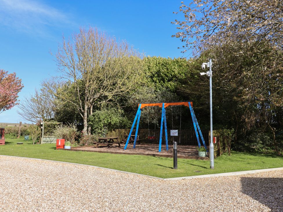 A swing set and benches in an outdoor area at Hazelwood 3 in Pinewood Retreat in Rousdon near Lyme Regis