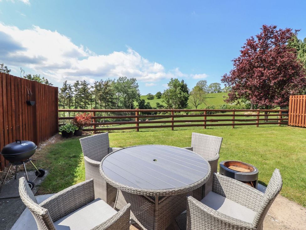 A garden with a table and chairs and a grill at Ysgubor Fachwen in Newtown