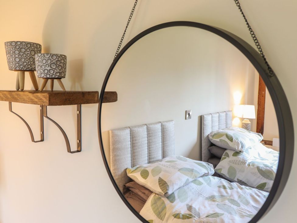 A bedroom with a mirror reflecting a bed and decorative items at Ysgubor Fachwen in Newtown