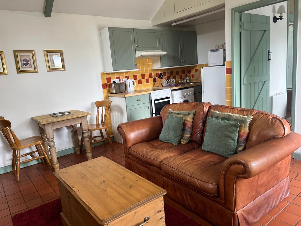A living room with a sofa, table, chairs, and kitchen area at Warbler Cottage near Cowbridge