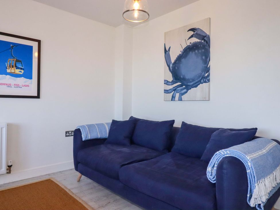 A living room with a blue sofa and crab artwork at Serfaus in Perranporth