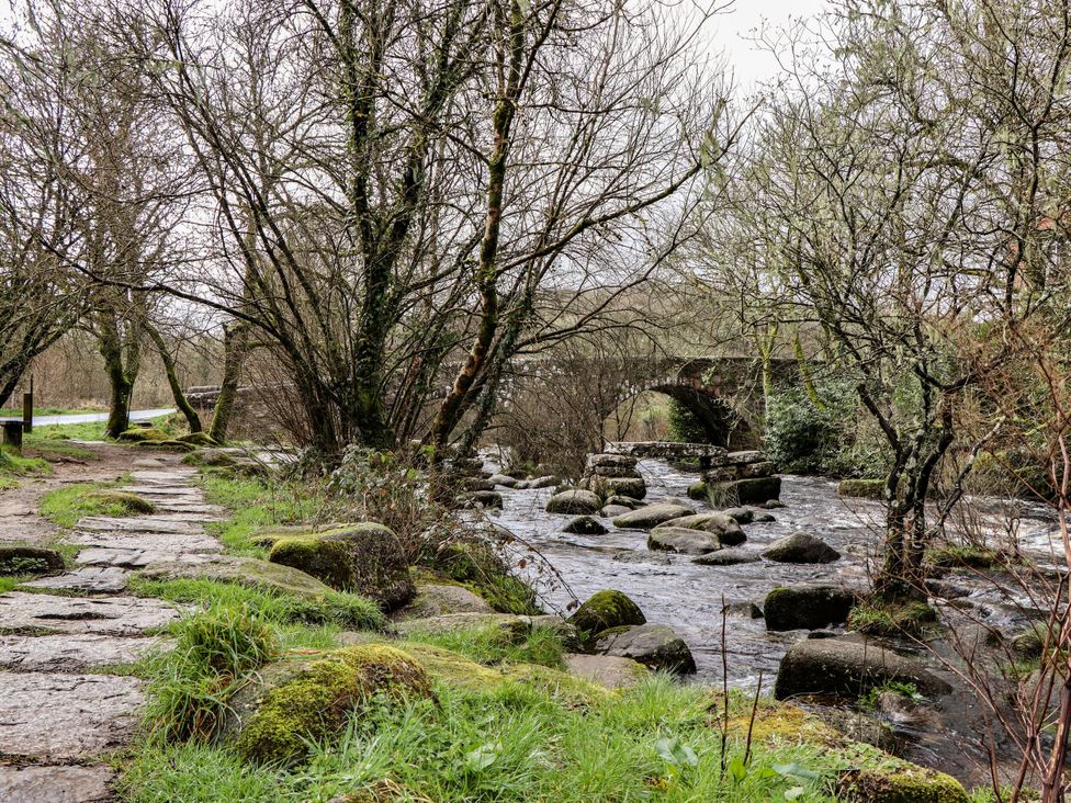 A pathway by a river with trees and a bridge in the background at The Apple Loft in Exeter
