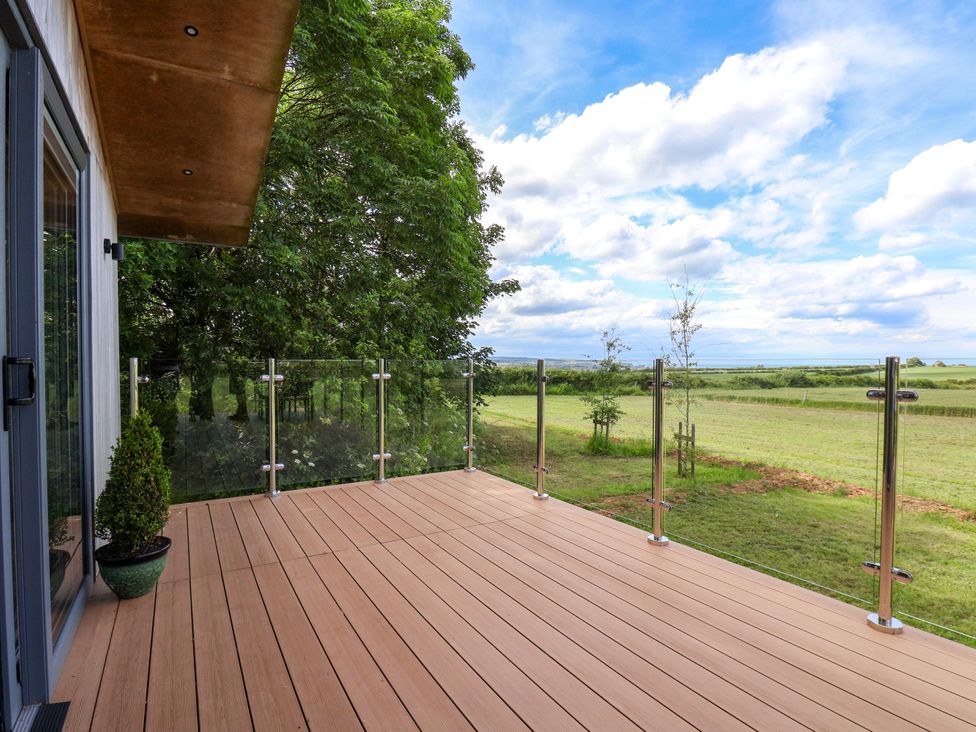 A deck area with glass railing and a view of trees and grass at Freedom Lodge @ Summerfield Farm in Whitby
