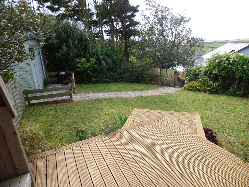 A garden with grass, decking, and a pathway at Trelake Cottage