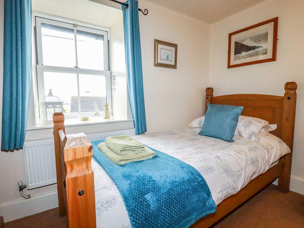 A bedroom with a single bed and blue curtains at Trelake Cottage in Tintagel