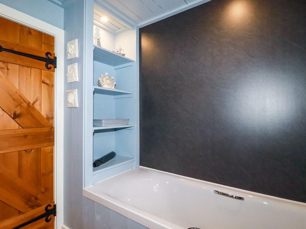 A bathroom with a bathtub and shelves at Trelake Cottage in Tintagel