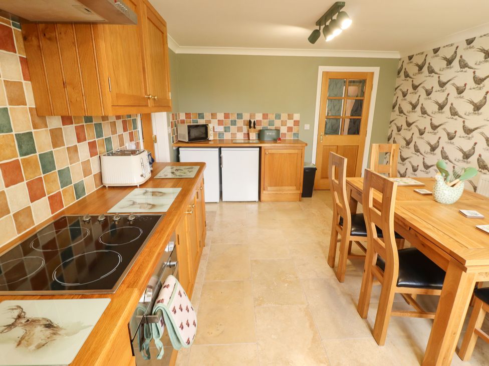 A kitchen with wooden cabinets and dining table at Rowan Cottage in Mareham-Le-Fen