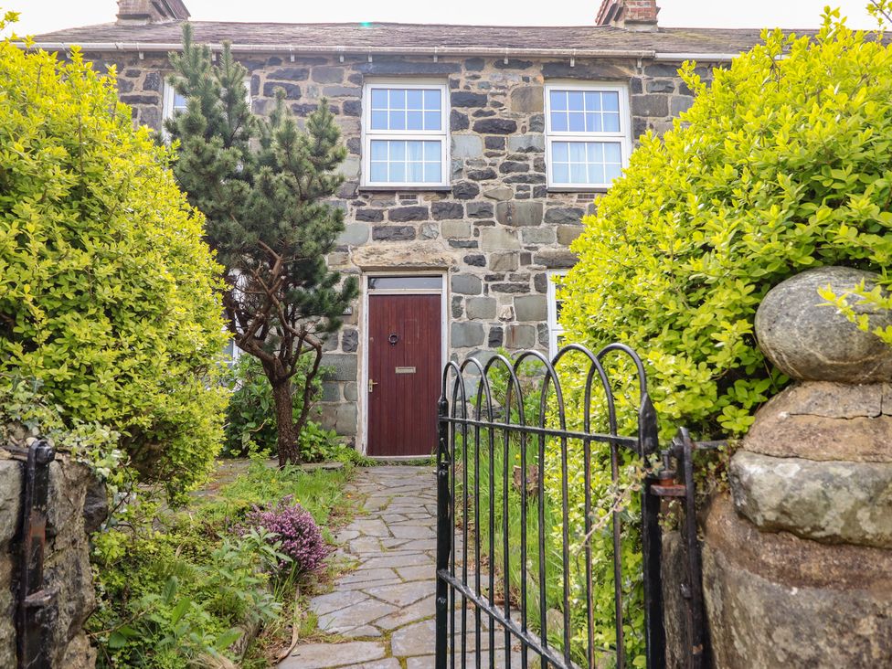 A stone house with a front door and pathway surrounded by bushes and trees at Glanrafon