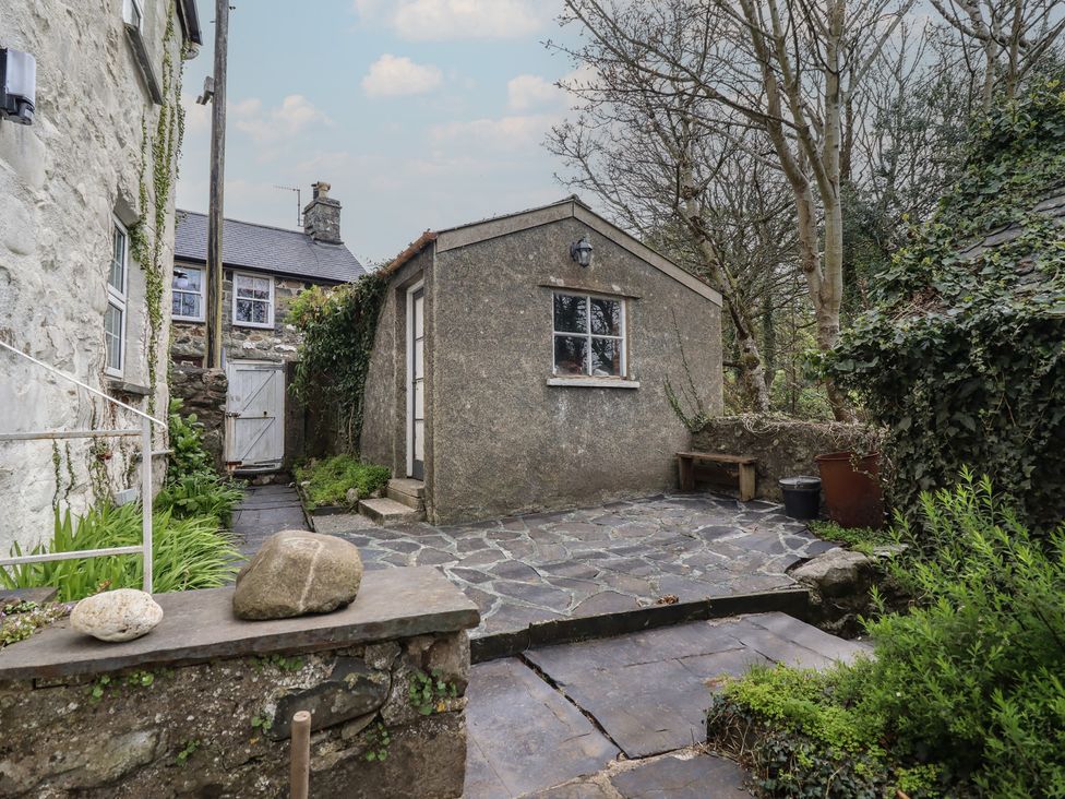 A garden area with a stone wall and a shed in Glanrafon