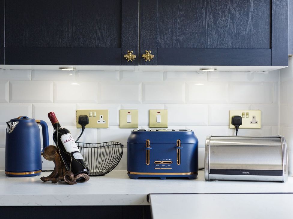 A kitchen with a kettle, wine bottle, toaster, basket, and bread bin at Admirals home