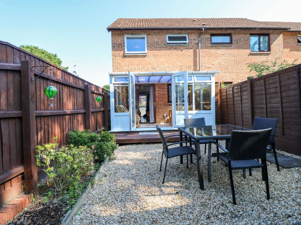 A garden with a table and chairs leading to a conservatory at 73 Pennywell Gardens New Milton